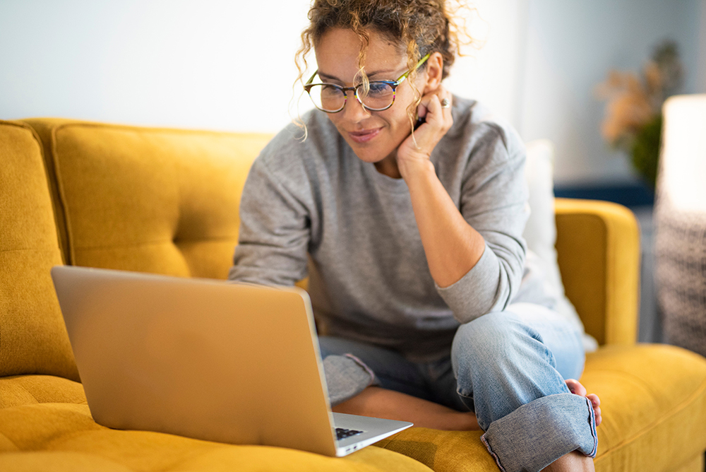 Woman with laptop on couch at home.