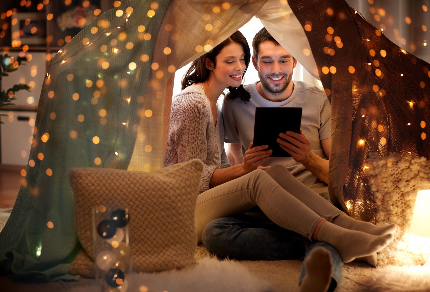 Man and woman cuddling while reading a tablet under sparkly lights.